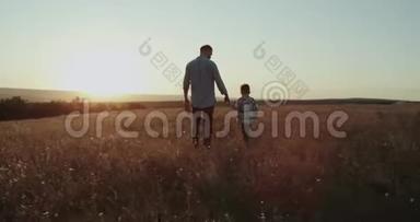 爸爸带着他的男孩，在夕阳下穿过田野，爸爸拿着网球拍。 在红色史诗上拍摄。 4k